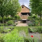 A garden setting with native plantings surrounding a simple barn structure, creating a functional outdoor space that blends naturally with its surroundings.