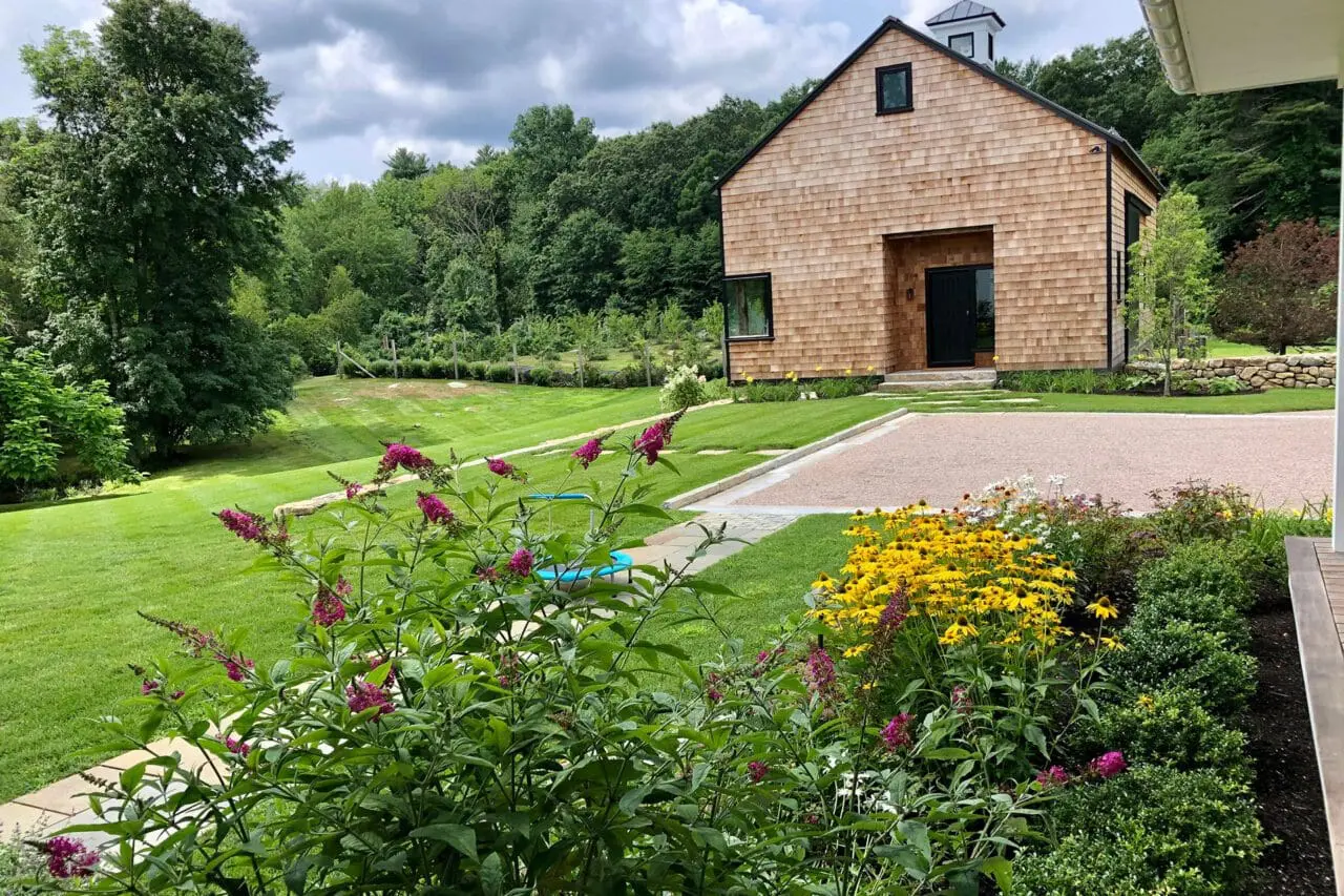 A landscaped garden with native plantings and flowering perennials surrounding a modern cedar-shingled home, blending structure with a natural setting.