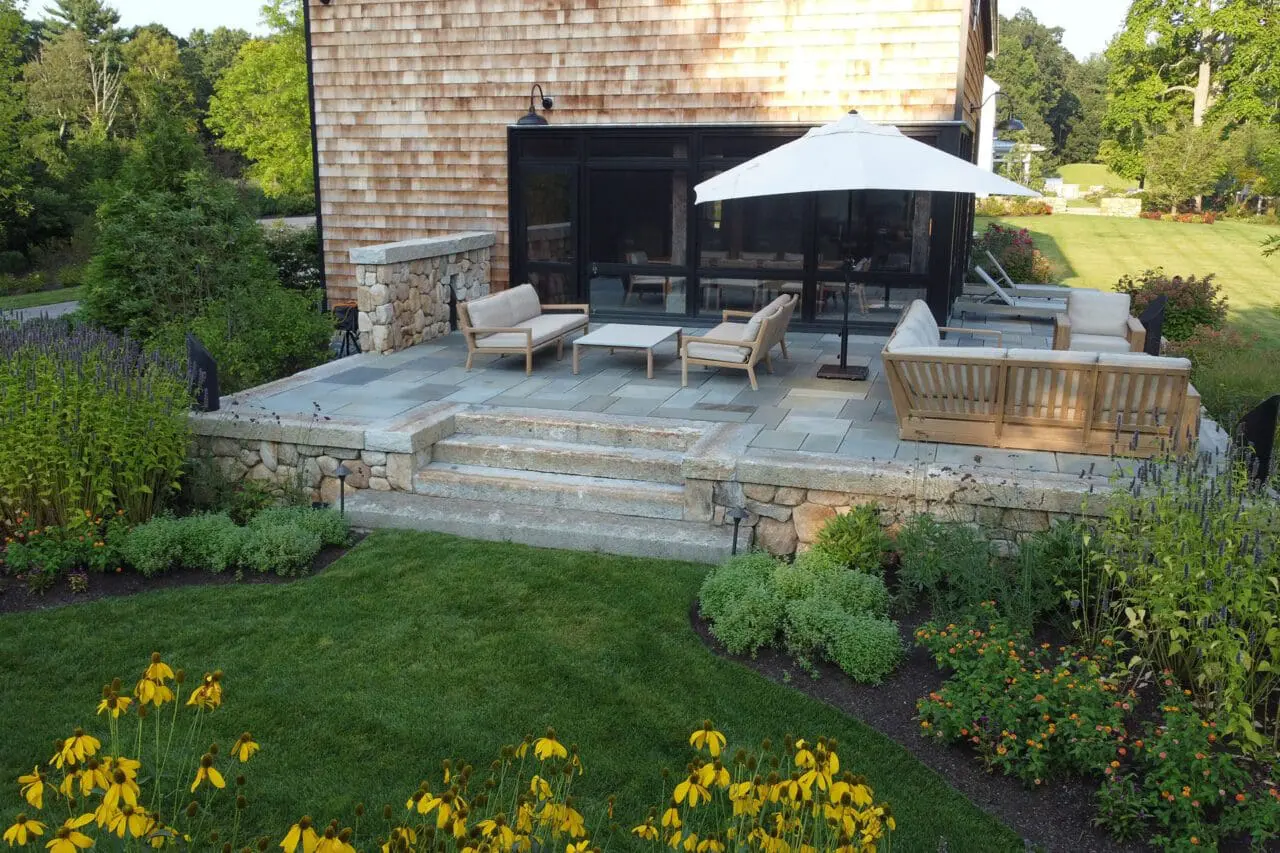 A stone patio set within a sustainable landscape, combining natural materials and surrounding plantings to create a durable, low-maintenance outdoor space.