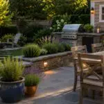 Lush Wayland, MA backyard with a stone patio, pool, outdoor kitchen, fire feature, and layered planting designed for comfortable summer outdoor living.
