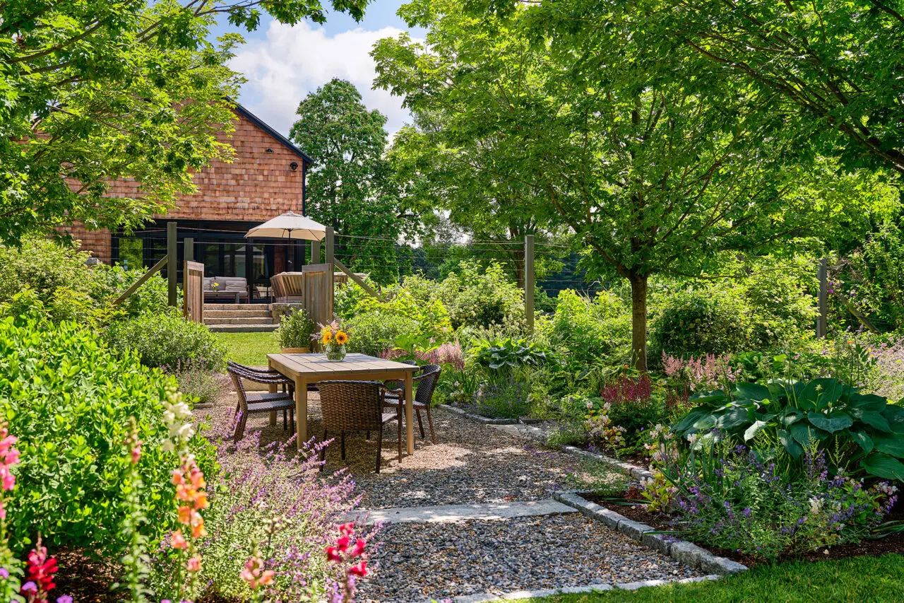 A gravel dining terrace sits within flowering borders, creating an inviting space for outdoor meals tied to the surrounding gardens. Photo: Sean Litchfield
