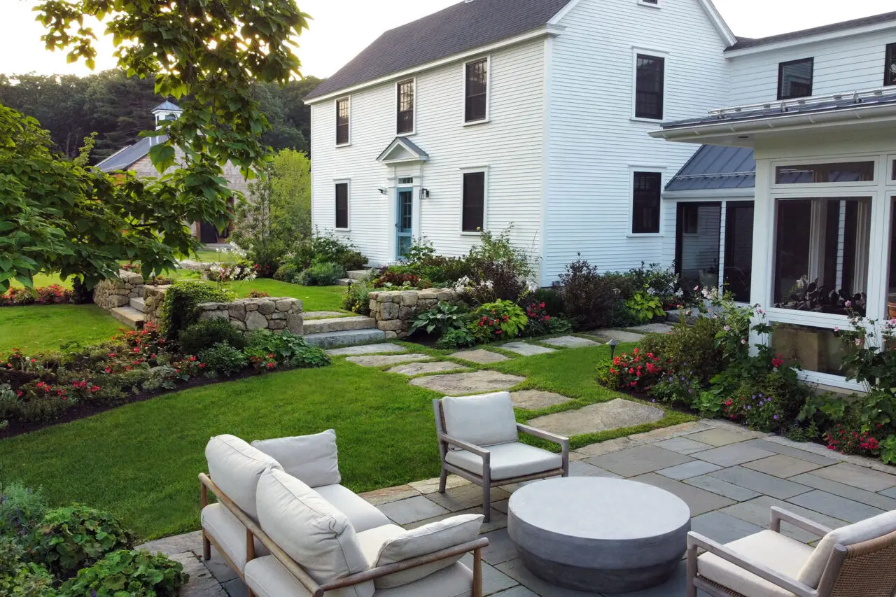 A stone terrace steps down to an open lawn, preserving long views while reinforcing the farmhouse’s historic character through restrained materials and balanced proportions.