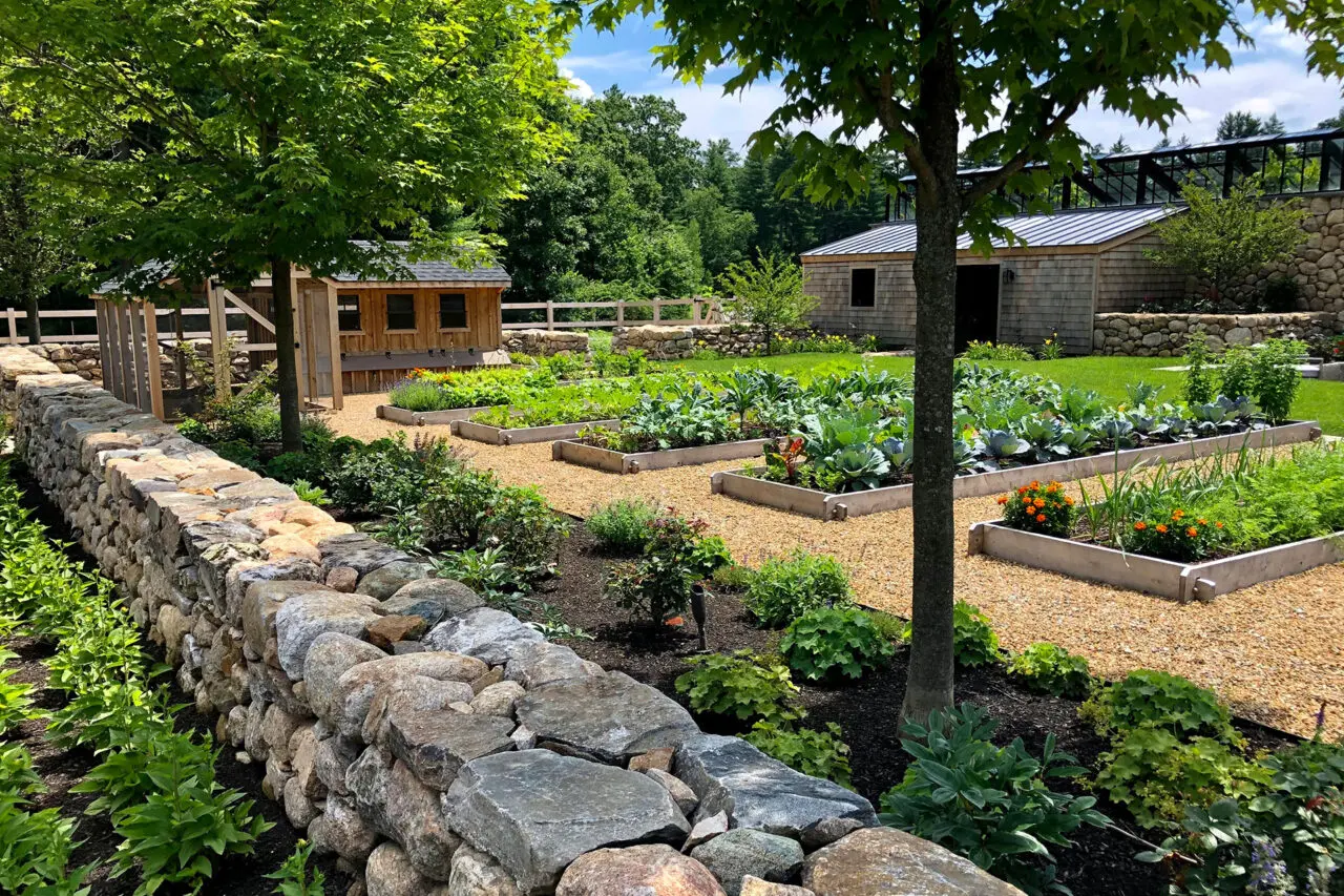Seasonal plantings fill raised beds bordered by stonework, showcasing a productive landscape designed for beauty, access, and crop rotation. Photo: Sean Litchfield
