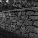 Acton, MA - A stone retaining wall leans outward, indicating movement and possible structural failure.