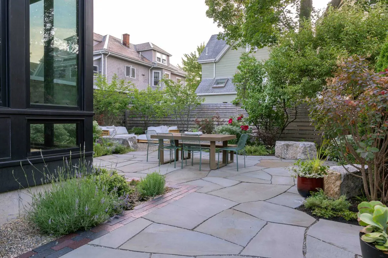 Irregular bluestone paving creates an organic foundation for outdoor dining, while layered planting establishes depth and enclosure within the compact footprint.
