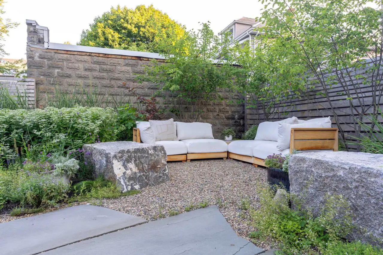A gravel seating area framed by reclaimed stone blocks offers a more intimate retreat, with native plantings providing texture and seasonal variation.