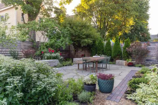 Large-format stone paving defines a flexible gathering space, with planting beds integrated to balance structure and softness throughout the patio.