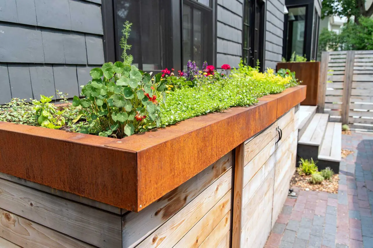 Weathering steel planters paired with custom wood cabinetry create a functional outdoor kitchen zone, with edible plantings positioned for easy access.