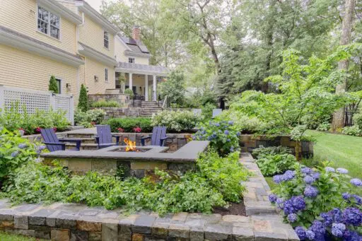 A natural stone fire feature anchors this lower terrace, where hydrangeas, layered perennials, and masonry walls shape a comfortable gathering space, copyright: Michael J Lee