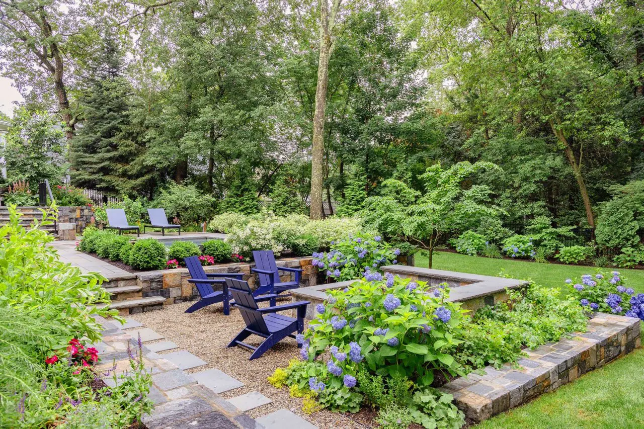 This gravel fire pit terrace is softened by hydrangeas and layered planting, offering a relaxed gathering space set slightly apart from the pool, copyright: Michael J Lee