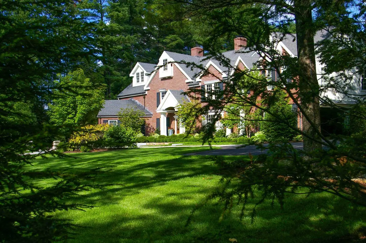 Wellesley Hills, MA - A broad, manicured lawn creates a lush foreground for this property, framed by mature trees and layered foundation plantings.