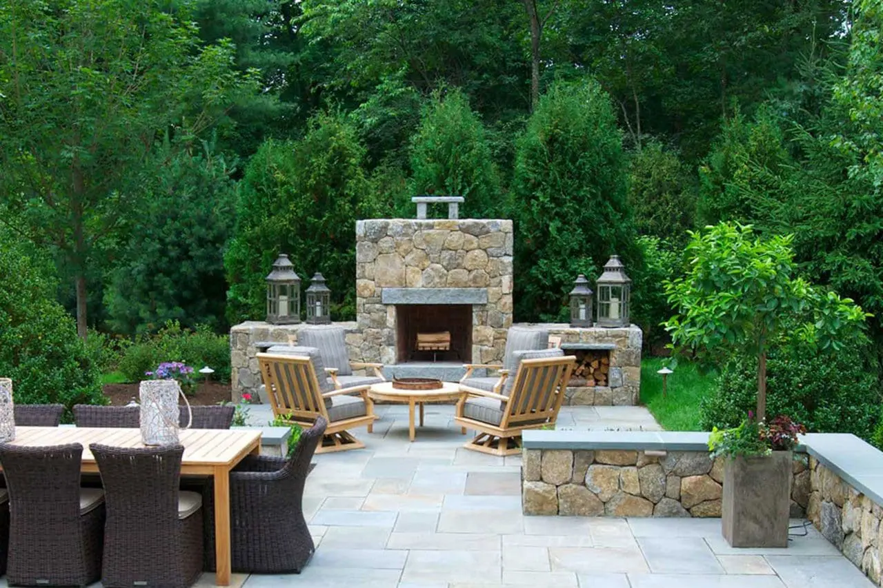 A stone outdoor fireplace anchors this patio dining and seating area, creating a comfortable destination for entertaining within a lush, private garden setting.