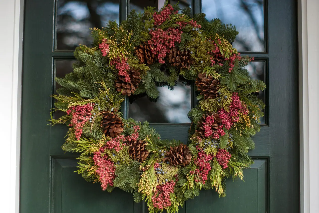 Fresh evergreen wreath with winter berries adds natural color and understated holiday charm, complementing classic New England entry doors.