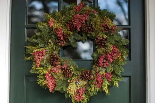 Fresh evergreen wreath with winter berries adds natural color and understated holiday charm, complementing classic New England entry doors.