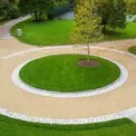 This circular gravel driveway features a cobblestone ring and planted center island, organizing traffic flow while adding visual focus and texture.
