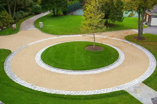 This circular gravel driveway features a cobblestone ring and planted center island, organizing traffic flow while adding visual focus and texture.