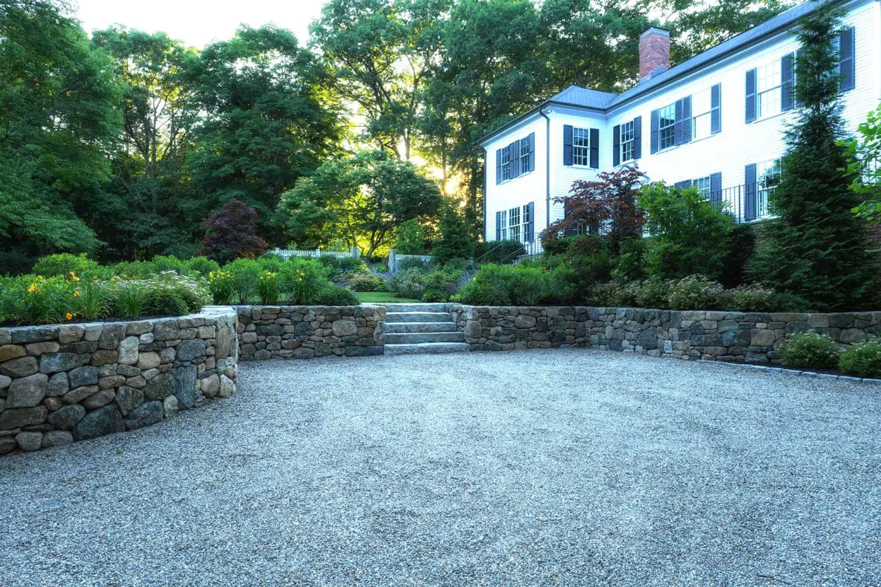 This formal gravel court is supported by stone retaining walls, organizing circulation and grade changes while reinforcing the stately character of a colonial estate.