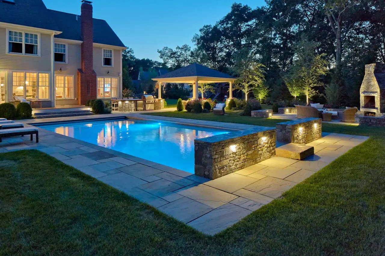 Landscape lighting adds warmth, depth, and definition, making the pool, stonework, and surrounding trees more inviting after dark.