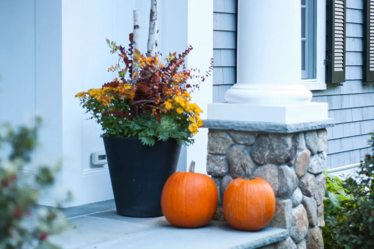 A black entry planter filled with fall mums, berries, and pumpkins accents a stone column, adding color and structure to the entryway.