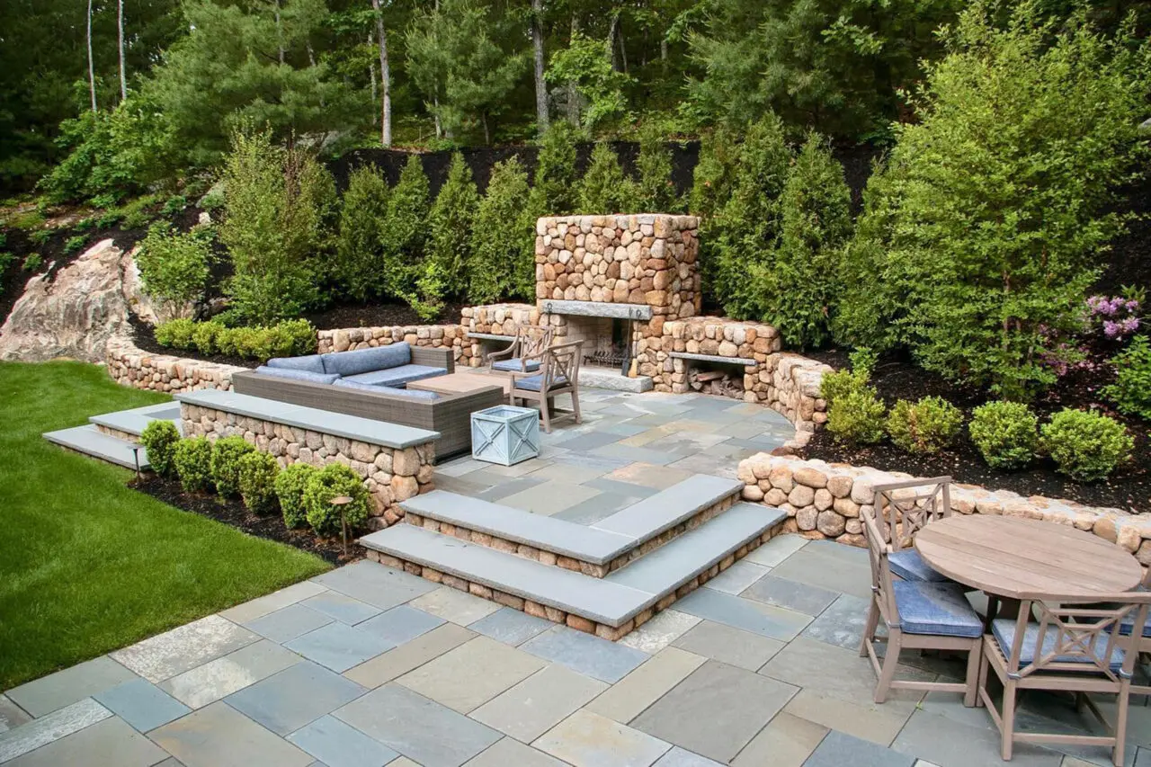 This formal outdoor fireplace constructed of natural stone adds symmetry and structure to the landscape, creating a refined outdoor room designed for comfort and entertaining.