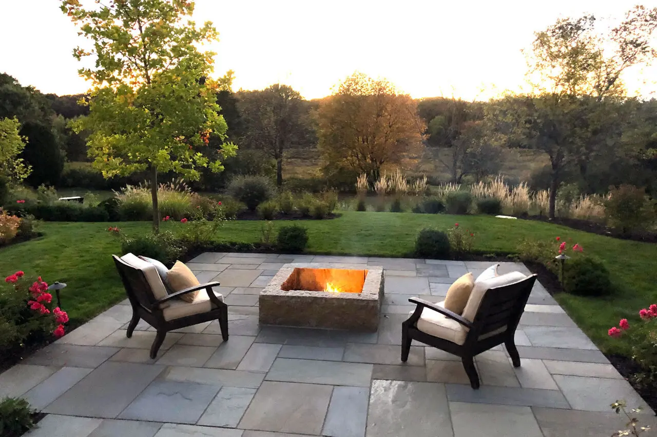 A minimal stone fire pit placed along an open lawn edge preserves long views while creating a subtle destination for quiet evenings and informal outdoor seating.