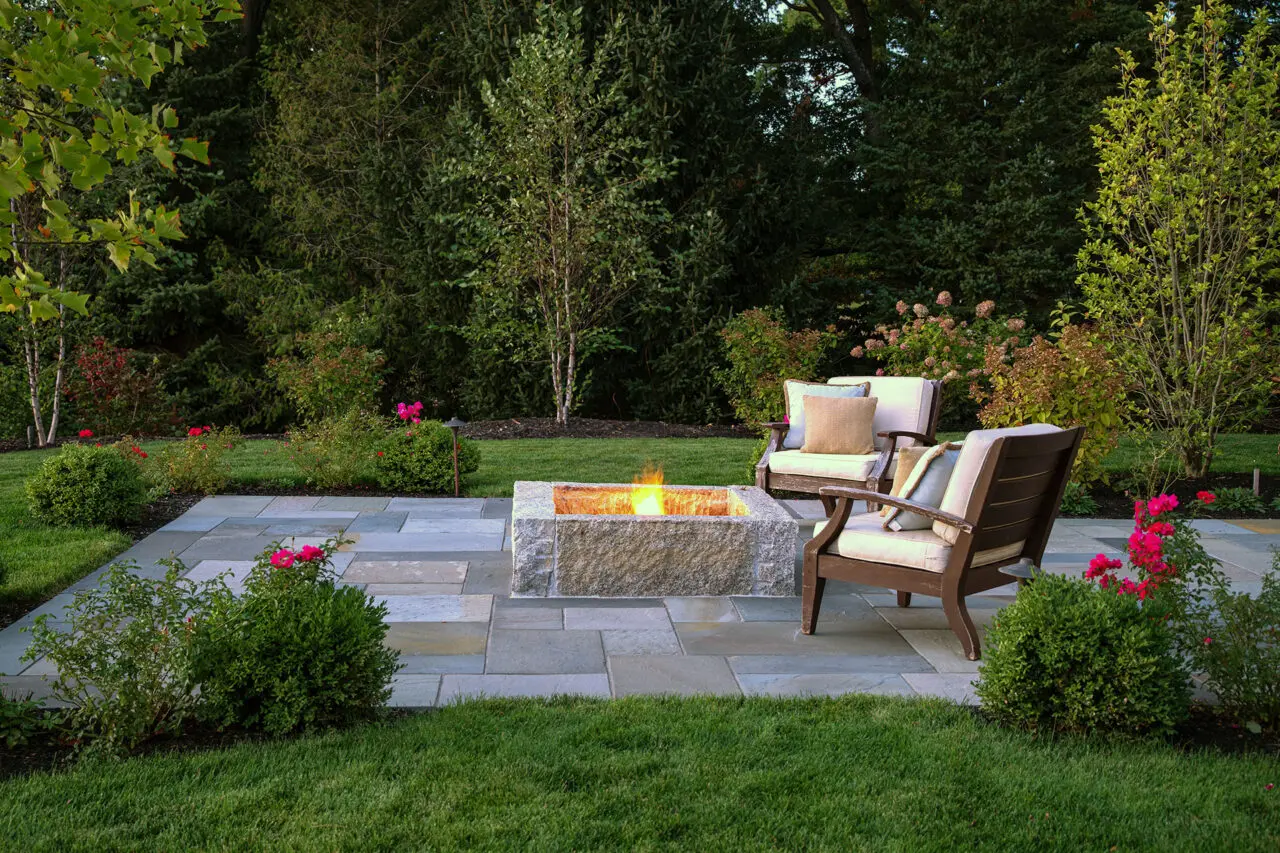 This rectangular granite fire pit in Winchester, MA anchors a bluestone patio with clean lines and lasting materials, creating a refined gathering space that complements the surrounding garden.
