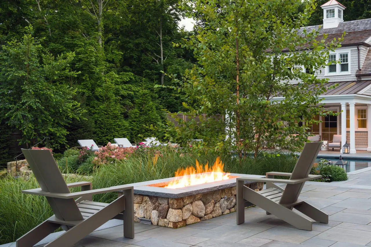 Positioned poolside, this rectangular stone fire pit adds warmth and visual balance, extending the usability of the patio while reinforcing clean lines within the landscape design.