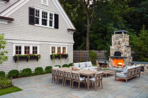 Outdoor dining space combining a stone fireplace and grill, extending usability into cooler evenings with warmth and visual focus.