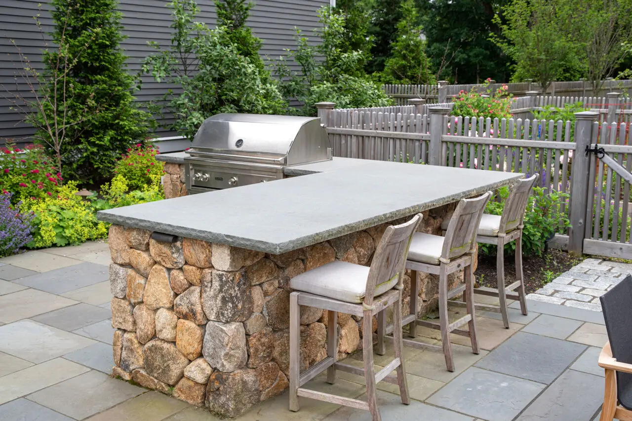 Custom stone patio designed for outdoor cooking, featuring a grill positioned near dining areas for easy serving and casual backyard meals.