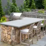 Custom stone patio designed for outdoor cooking, featuring a grill positioned near dining areas for easy serving and casual backyard meals.