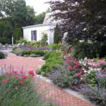 A brick garden path flows through lush perennials, blending structure with classic estate-style planting.