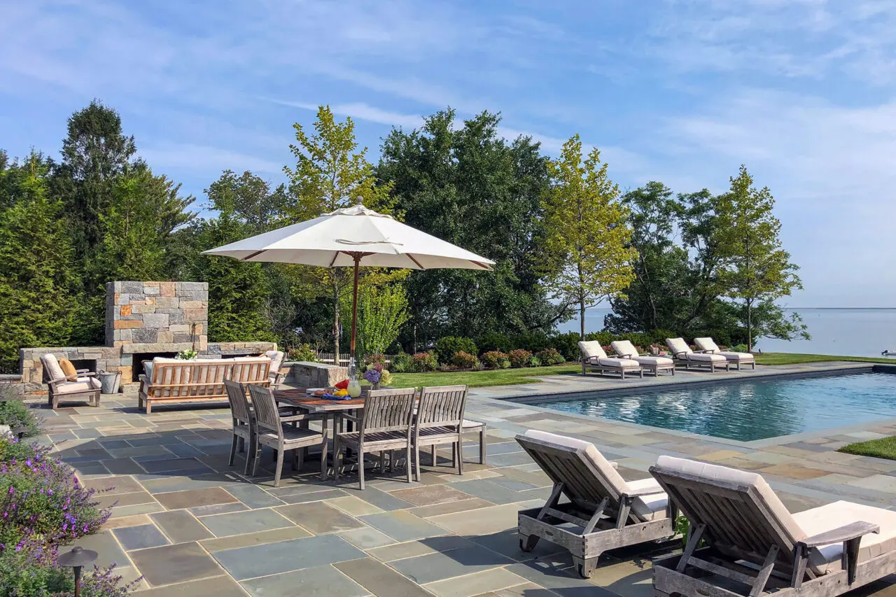 Poolside bluestone patio with dining table and serene water views blends functional outdoor dining with scenic coastal atmosphere.