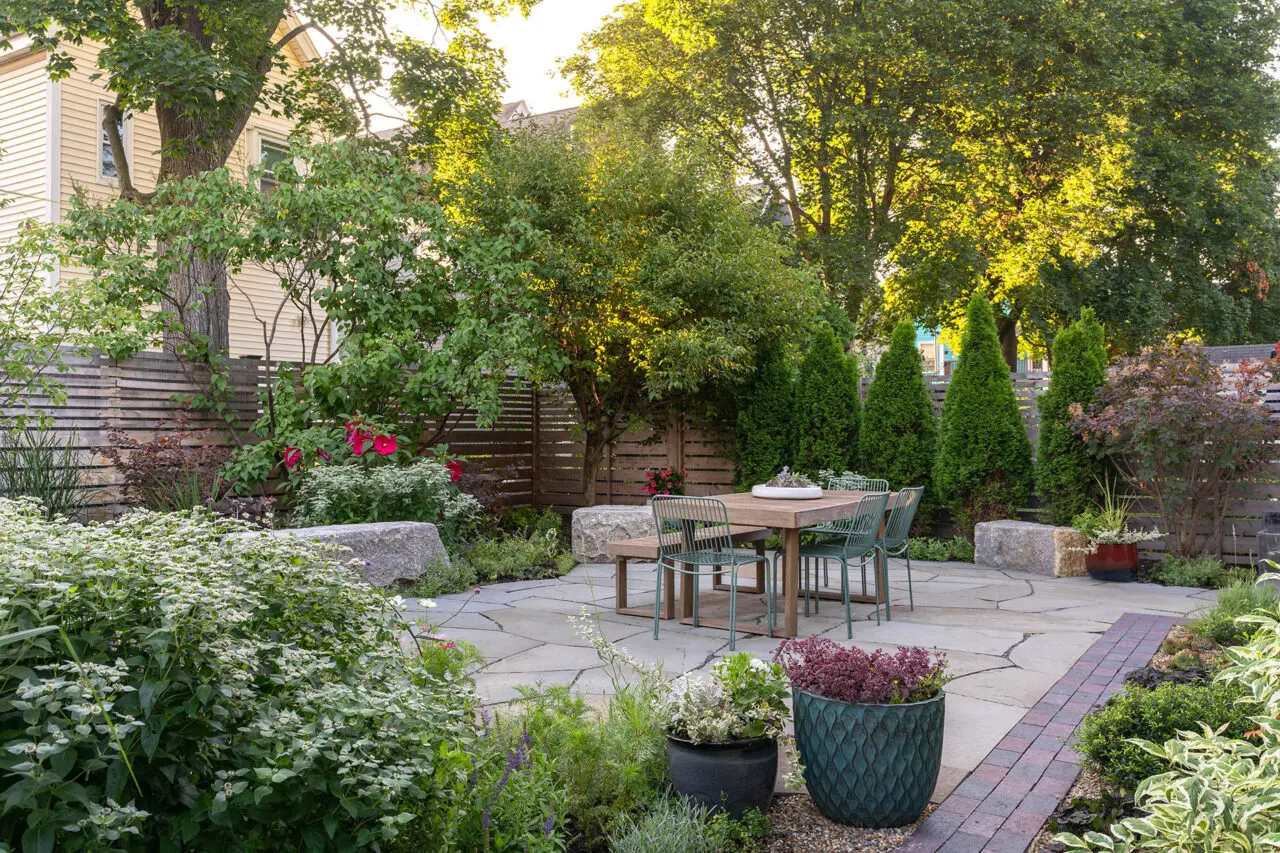 Small garden patio with lush perennial borders and privacy trees creates a serene urban escape with natural stone paving and cozy seating.