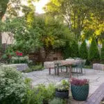 Small garden patio with lush perennial borders and privacy trees creates a serene urban escape with natural stone paving and cozy seating.