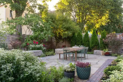 Small garden patio with lush perennial borders and privacy trees creates a serene urban escape with natural stone paving and cozy seating.