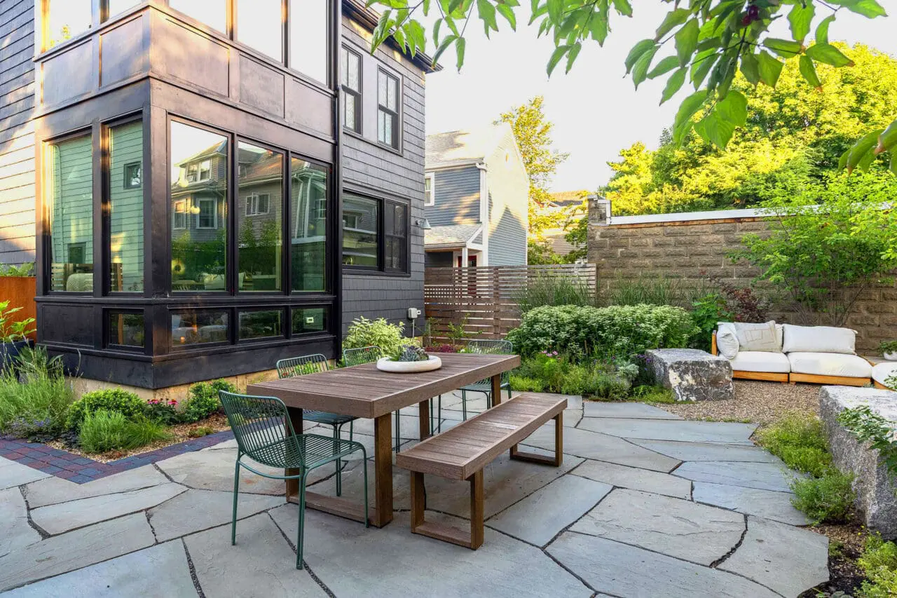 Irregular stone patio with modern furnishings defines this urban backyard terrace, creating a chic outdoor lounge that maximizes space and privacy in city gardens.