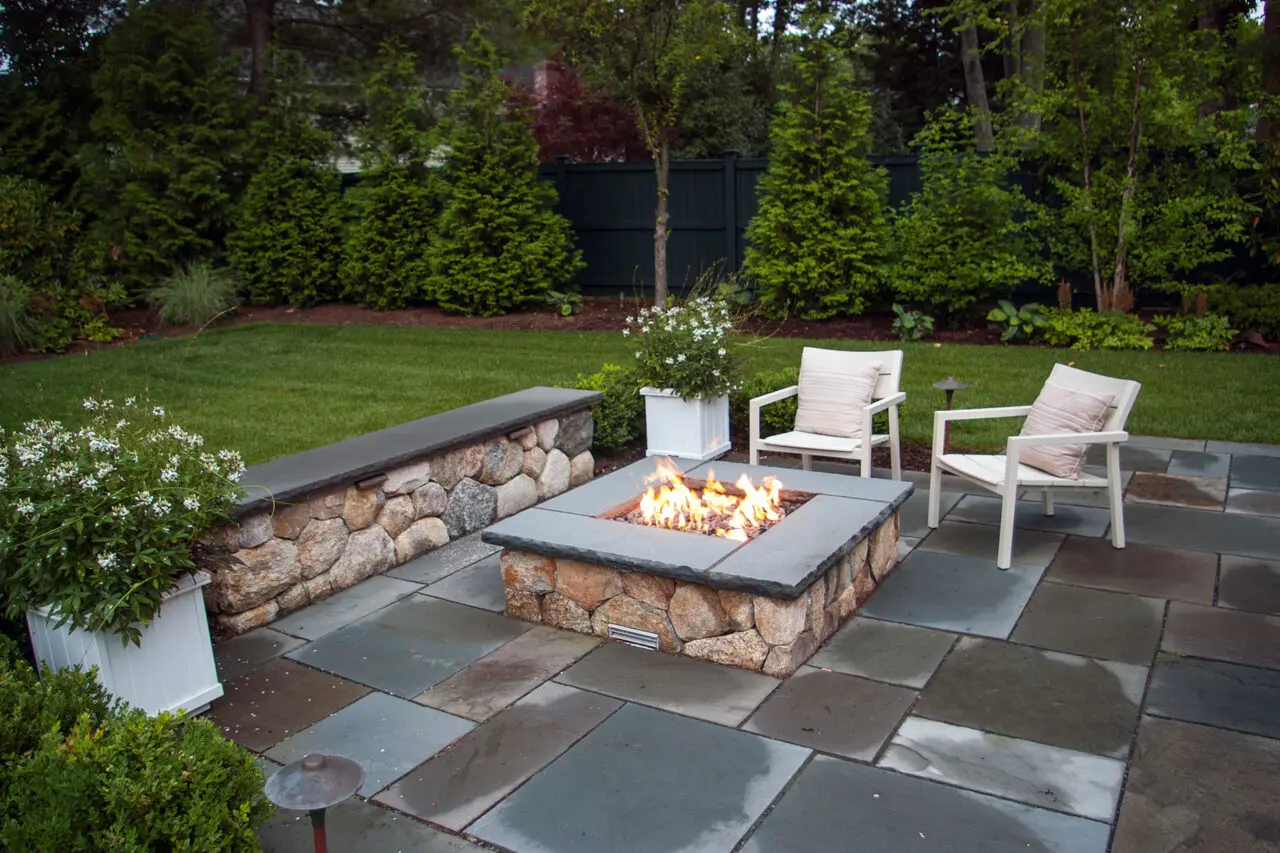 White box planters flanking a fire pit hold mixed shrubs, defining the space with year-round structure and simplified long-term maintenance.