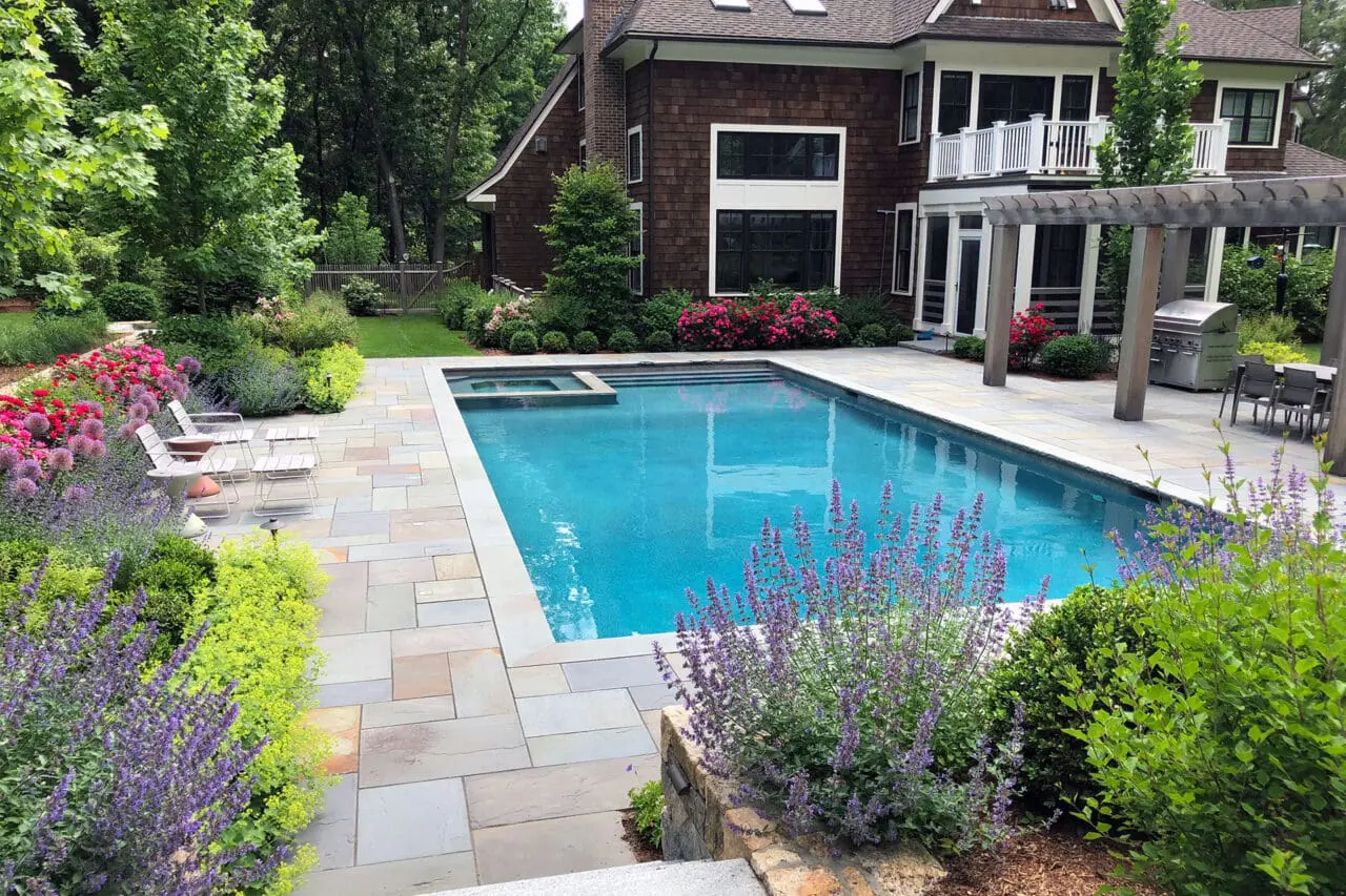 Surrounded by flowering borders and a bluestone patio, this rectangular pool blends formal structure with seasonal color, creating a garden-focused swimming environment.