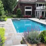 Surrounded by flowering borders and a bluestone patio, this rectangular pool blends formal structure with seasonal color, creating a garden-focused swimming environment.