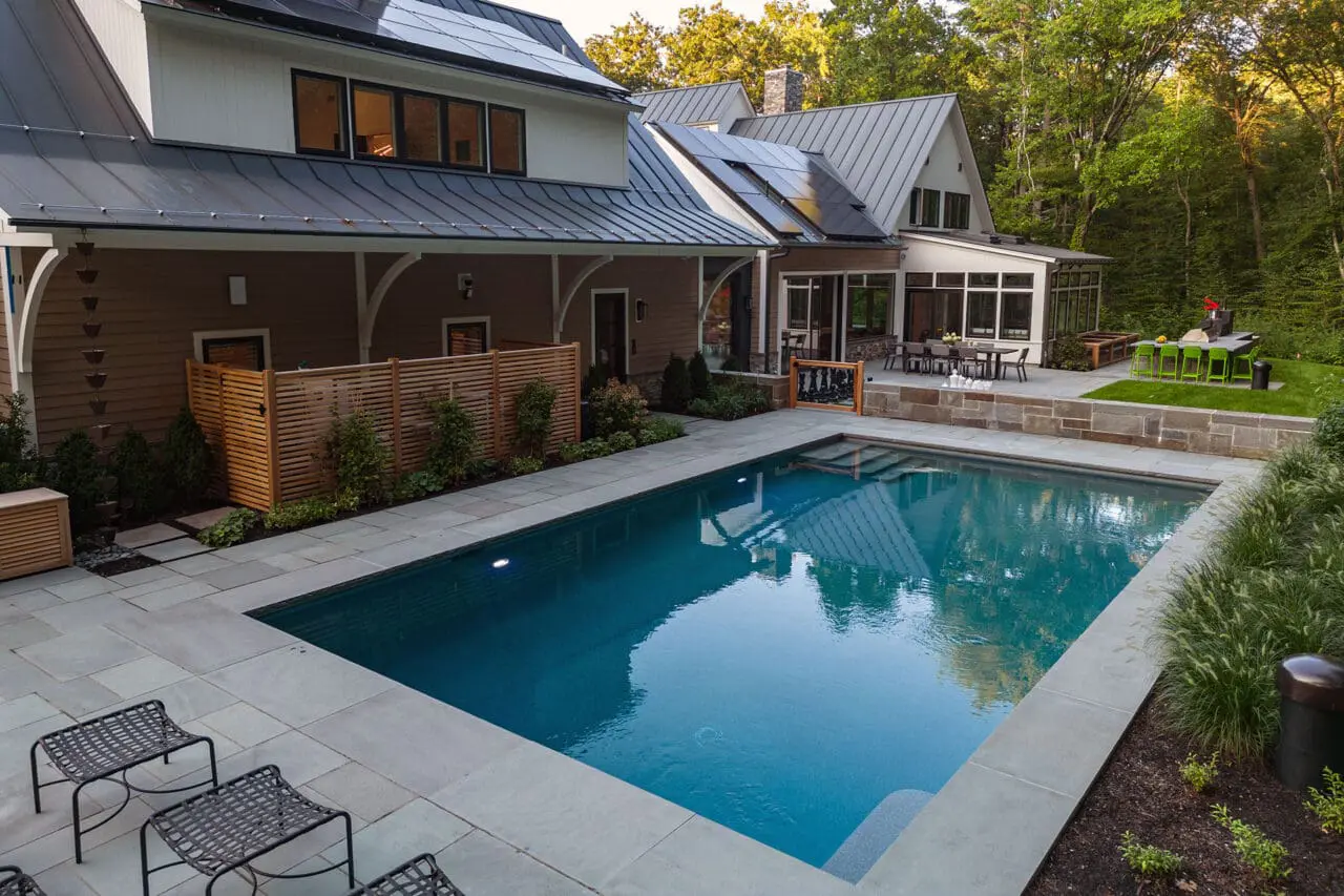 A formal rectangular pool framed by a stone patio and symmetrical planting, establishing a strong visual axis and an elegant focal point within a carefully organized backyard setting.