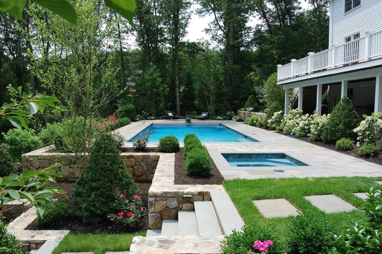 This pool design uses tiered stone retaining walls to manage grade changes, creating visual depth, structured seating edges, and a refined transition between pool and surrounding landscape.