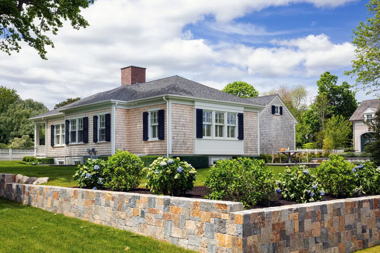 A cut stone garden wall borders hydrangea planting, using shrubs to soften the formal stone edge and add seasonal color.