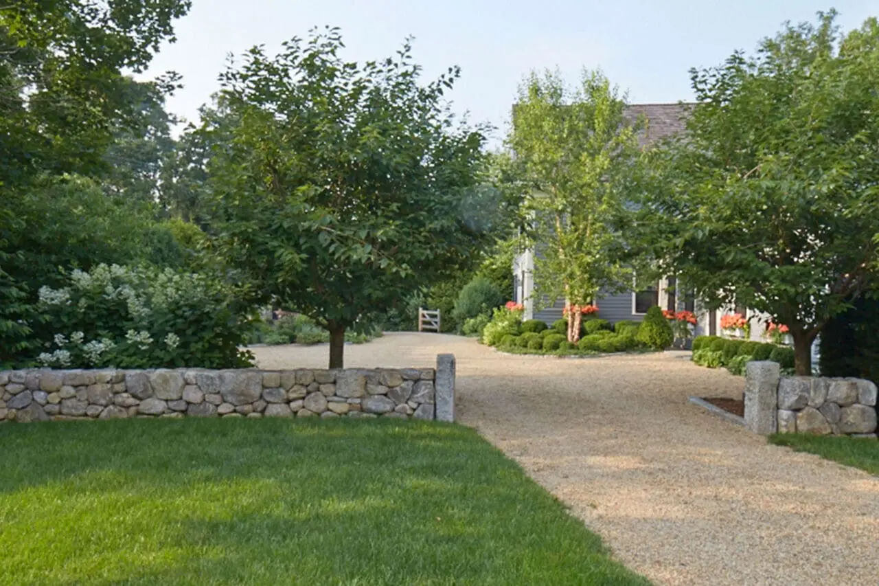 A fieldstone wall lines the driveway entry, using natural stone mass to define the approach and frame the gravel drive. © charles mayer photography