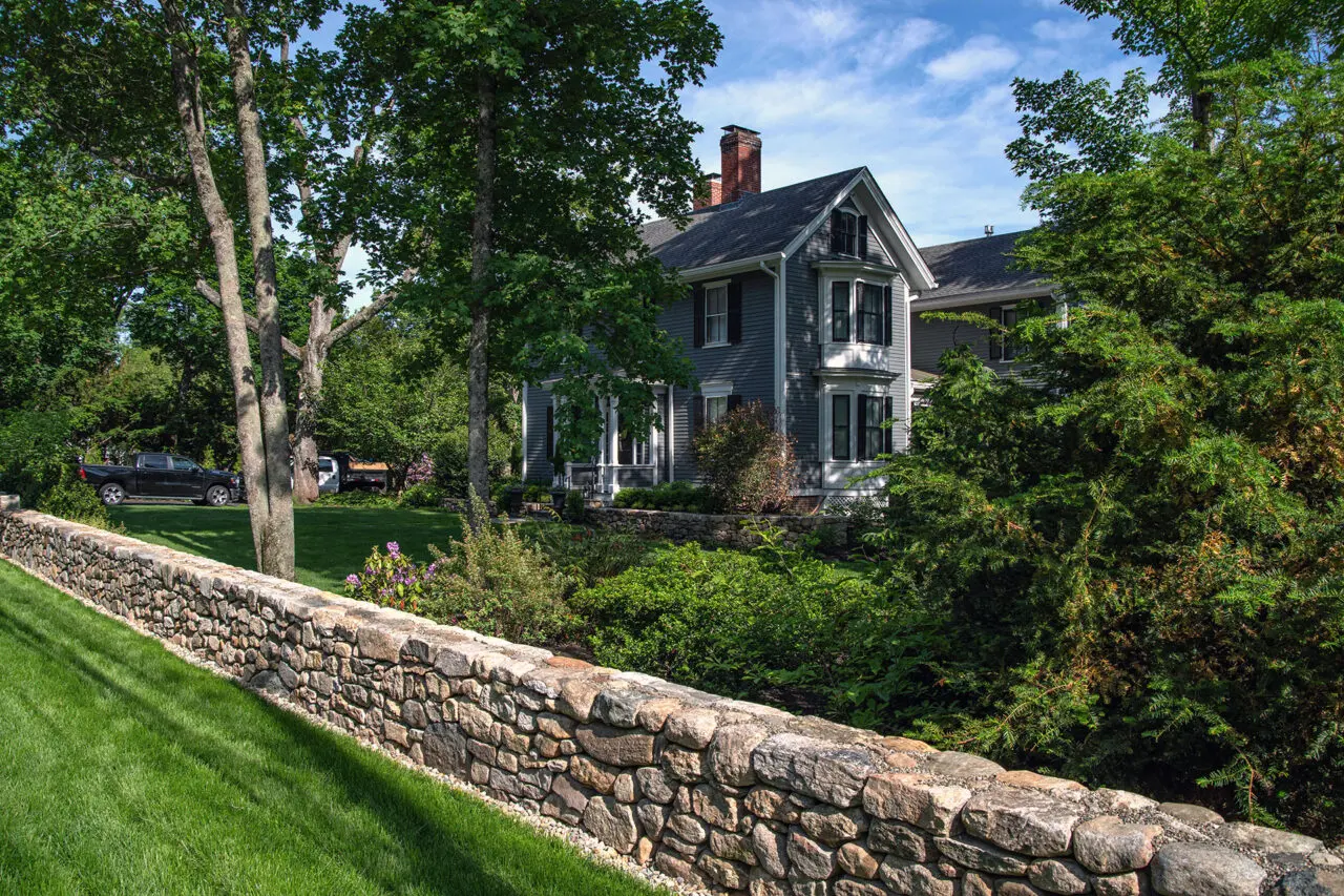 This front-yard fieldstone wall reinforces the traditional character of the home, with layered shrubs and hedges providing structure and curb appeal.