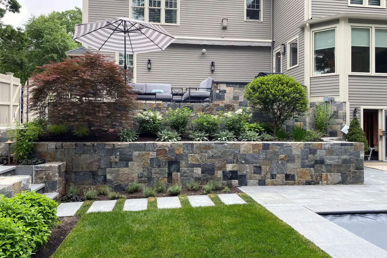 Granite block steps are integrated into a sloped retaining wall, with adjacent shrubs stabilizing the grade and visually tying the stonework into the landscape.