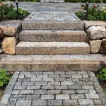 Granite steps descend to a cobblestone landing between fieldstone walls, with shrubs and hedges adding structure and refinement to this entry sequence in Weston.