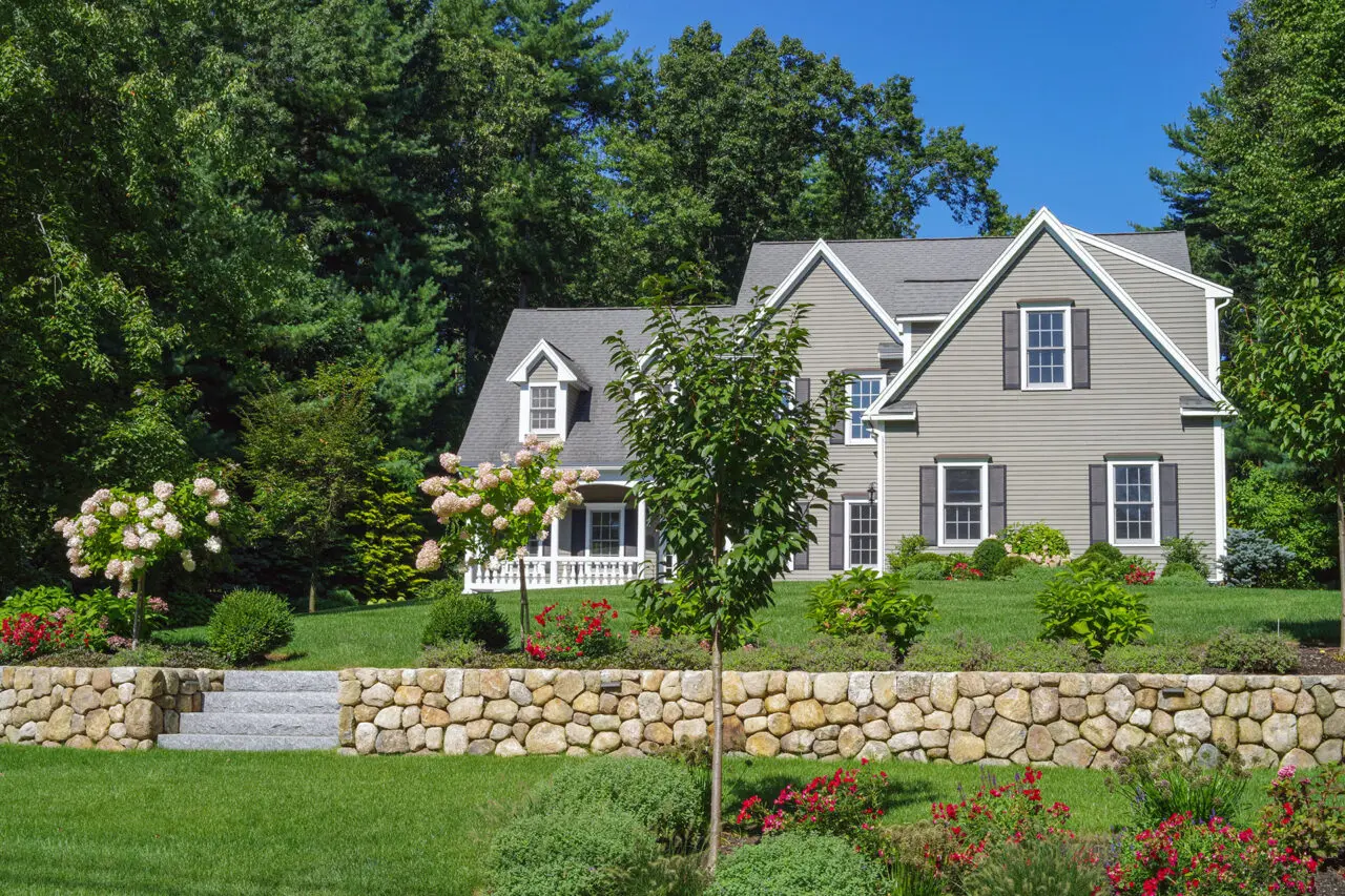 A low fieldstone retaining wall manages a gentle grade change in the front yard, its informal stonework complemented by shrubs that ease the transition between lawn and planting areas.
