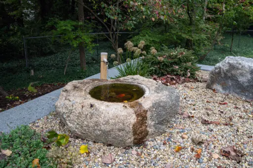 A carved granite bird bath fountain provides subtle water sound while supporting birds and wildlife, adding charm and ecological value to the garden.