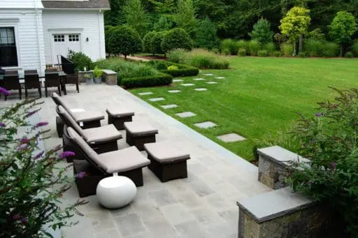 Weston, MA - Outdoor space designed for dining and gathering opens to an emerald green lawn bordered by lush planting beds.