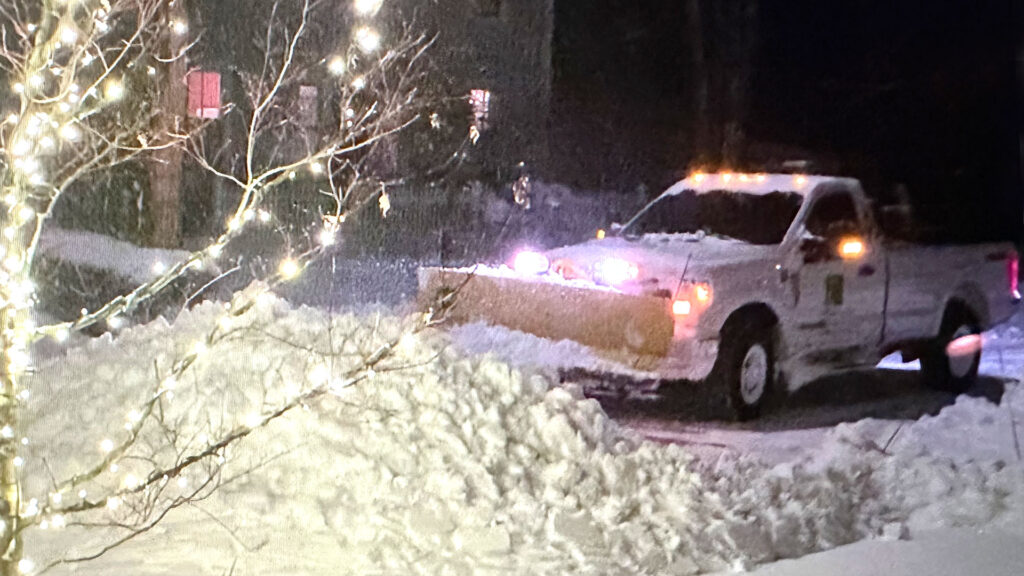 a Blade of Grass snow removal truck plows fresh snowfall from a residential driveway, pushing back deep snow banks to maintain safe, reliable access during a New England winter storm.